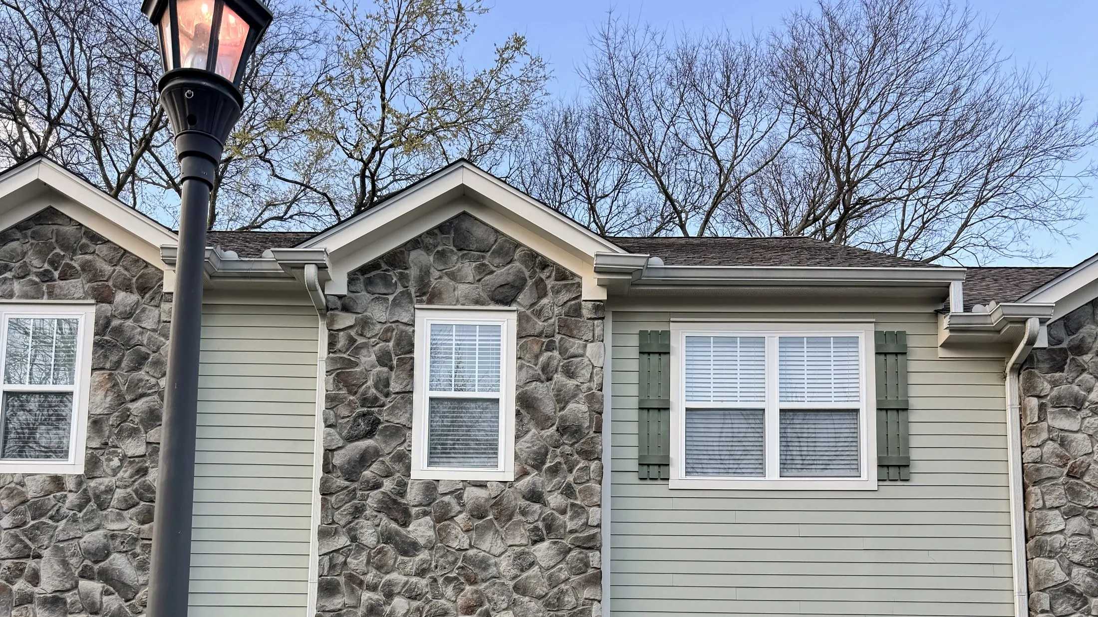 The 408 at Brookstone — sage siding, stone veneer, and a lit lamp on Alicia Drive